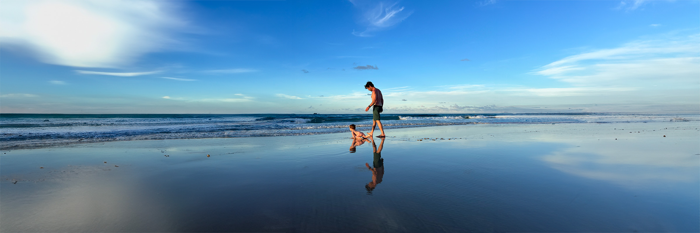 Josh and his daughter walking together on a reflective beach at low tide